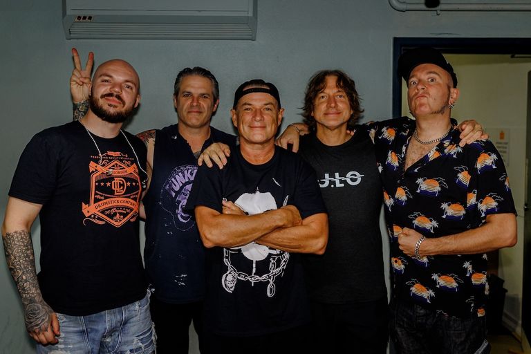 American rock band Ugly Kid Joe members posing together indoors with hands on each other's shoulders, smiling for a promo photo.